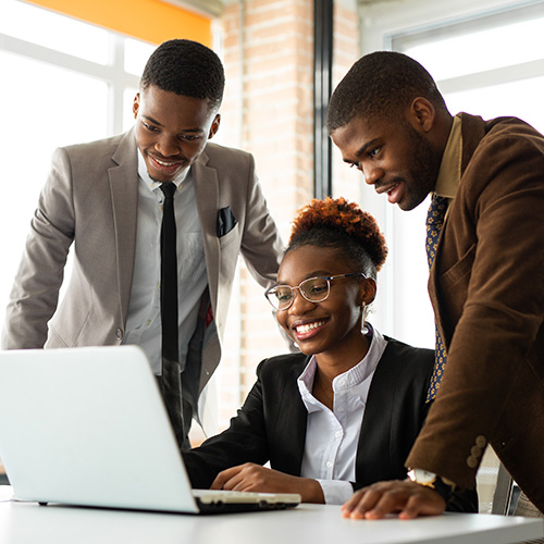 Young African American lady sitting in front of a laptop, 2 male colleagues standing besides her